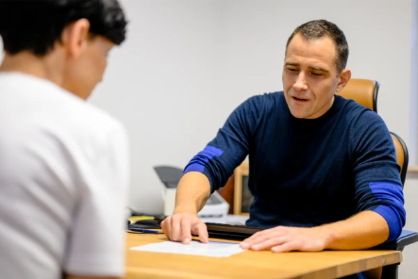 Man zeigt im Büro auf ein Hyaluronsäure-Knie-Dokument und bespricht Behandlungsoptionen mit einer weiteren Person.